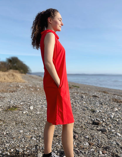 Woman in a red dress standing on a pebbly beach with ocean and sky in the background
