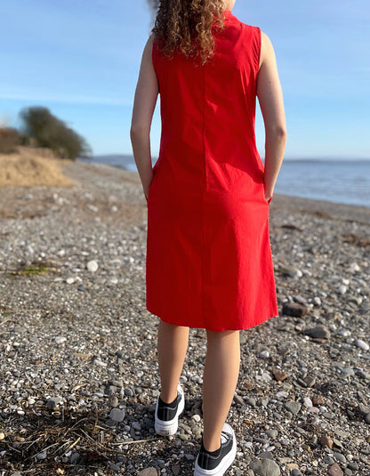 Person wearing a red dress standing on a pebbly beach with ocean view