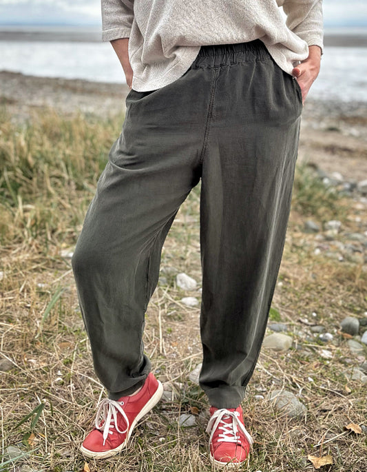 Woman standing outdoors in a natural setting wearing a cream organic cotton sweater and dark green tercel pants.