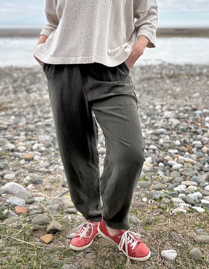 Woman standing outdoors in a natural setting wearing a cream organic cotton sweater and dark green tercel pants.