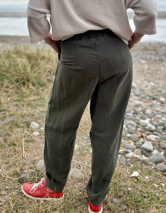 Woman standing outdoors in a natural setting wearing a cream organic cotton sweater and dark green tercel pants.