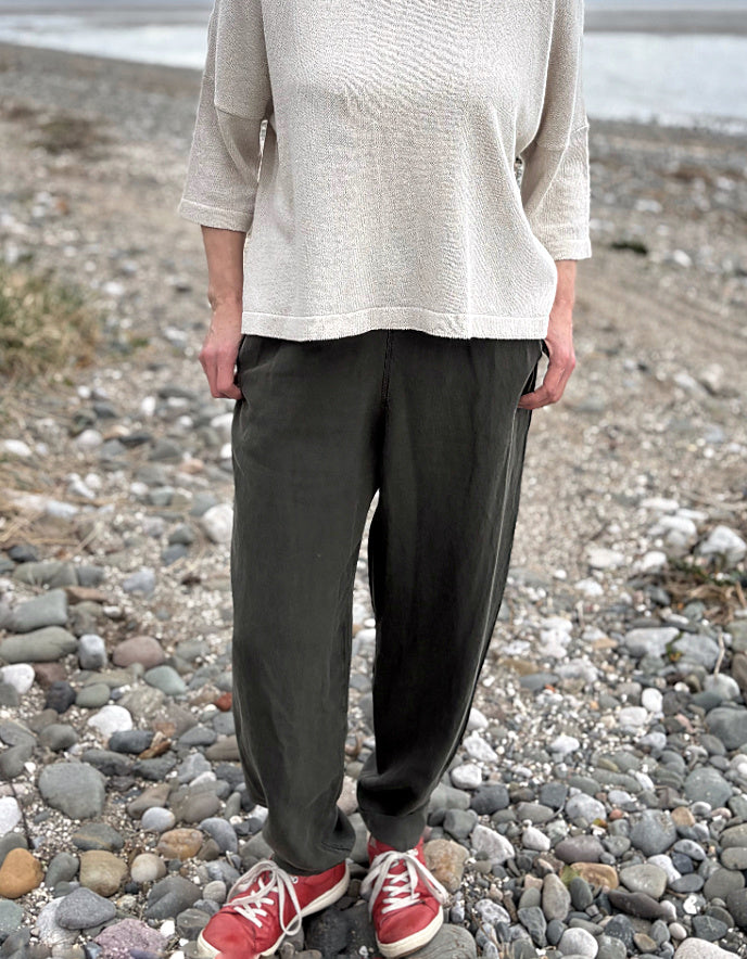 Woman standing outdoors in a natural setting wearing a cream organic cotton sweater and dark green tercel pants.