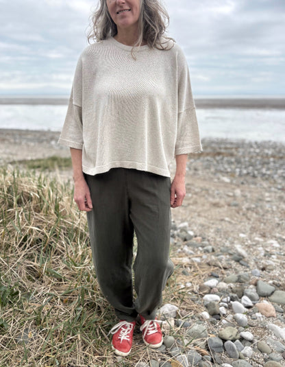 Woman standing outdoors in a natural setting wearing a cream organic cotton sweater and dark green tercel pants.
