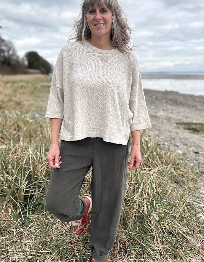 Woman standing outdoors in a natural setting wearing a cream organic cotton sweater and dark green tercel pants.