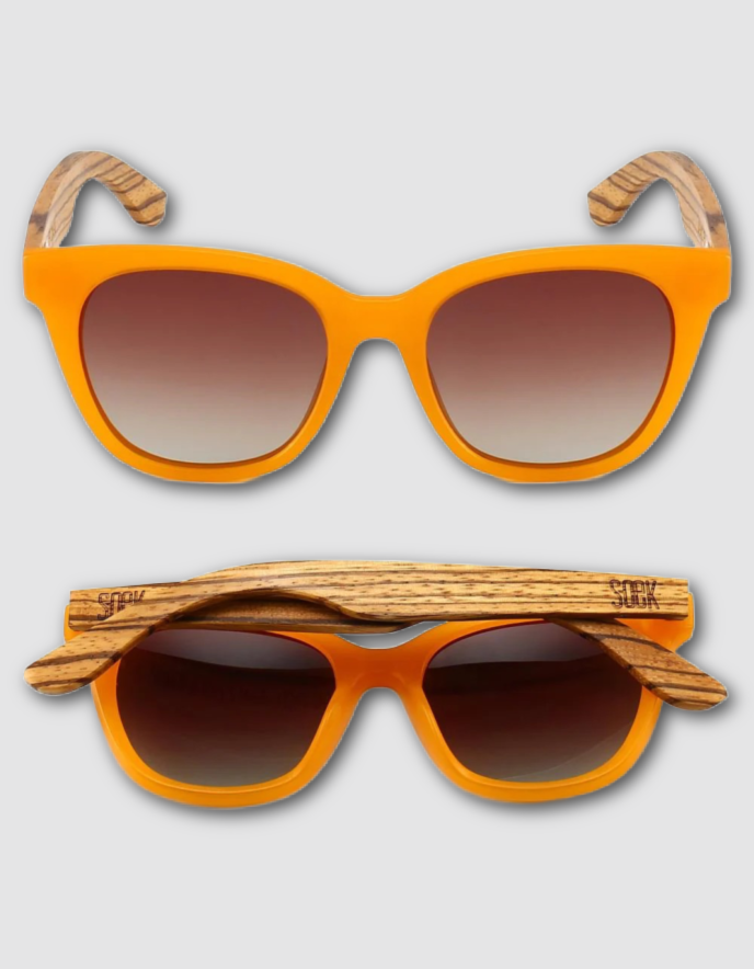 A pair of sunglasses shown from two angles on a light grey background. The sunglasses have a bright orange frame, gradient brown lenses, and a natural wood grain temple arm.