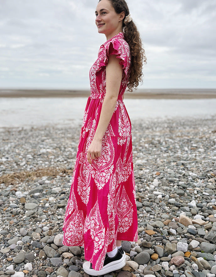 Woman in a pink dress standing on a pebbly beach with ocean in the background