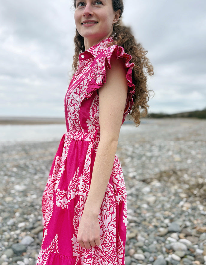 Woman in a pink dress standing on a pebbly beach with a cloudy sky.