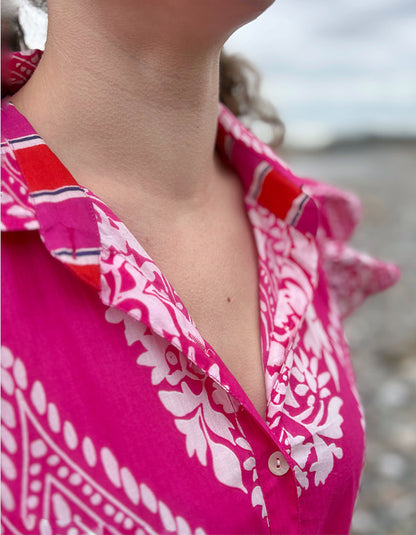 Close-up of a person wearing a bright pink patterned shirt with a blurred background