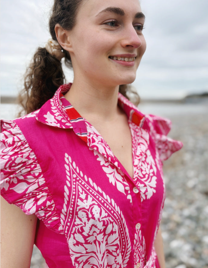 Woman wearing a pink and white patterned blouse standing on a beach.