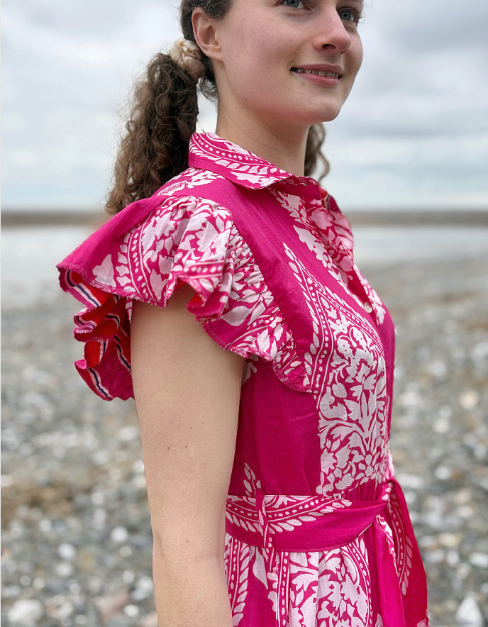 Woman wearing a pink and white patterned dress on a beach.