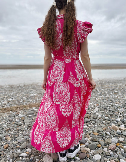 Person wearing a pink dress with white patterns on a pebbly beach.