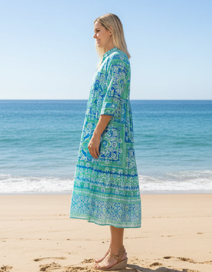 a woman wearing a turquoise layered cotton shirt dress with sleeves on a beach