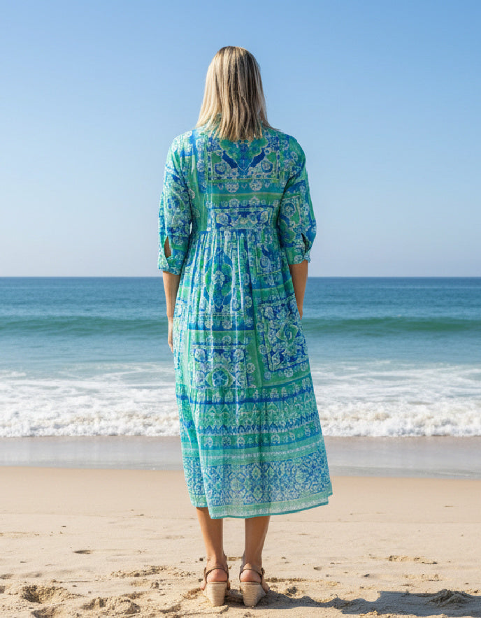 a woman wearing a turquoise layered cotton shirt dress with sleeves on a beach