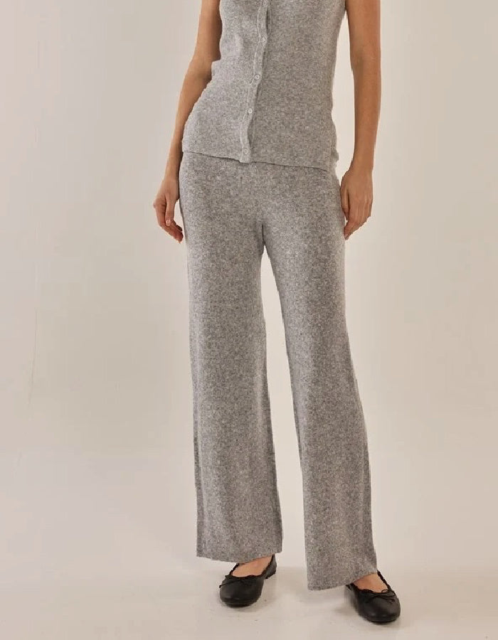 A model wearing a light gray knit matching set consisting of a sleeveless top and wide-leg pants, paired with black flats, against a plain light beige studio background.