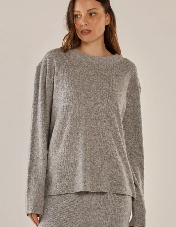 A woman wearing a heather gray knit sweater with a relaxed, oversized fit and long sleeves, paired with a matching gray knit skirt, set against a plain beige studio background.