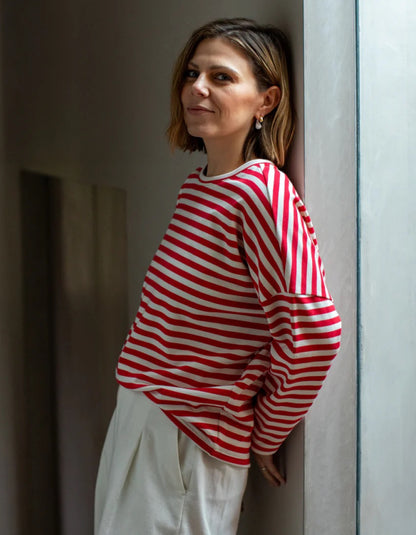 Woman wearing a red and white striped shirt leaning against a wall.