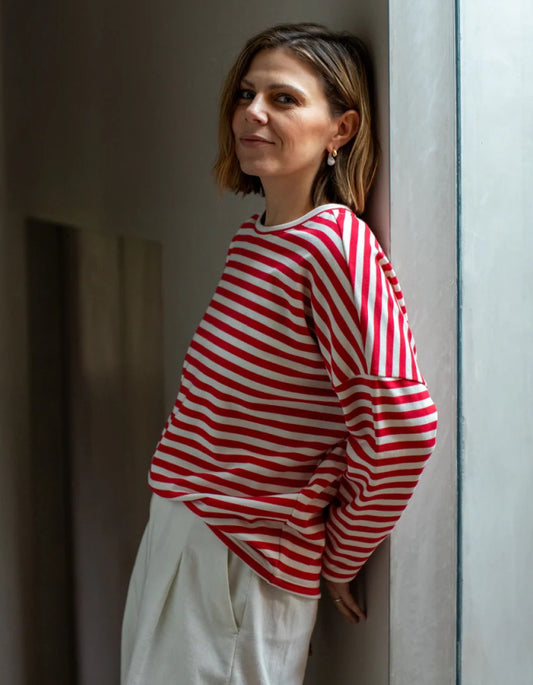 Woman wearing a red and white striped shirt leaning against a wall.