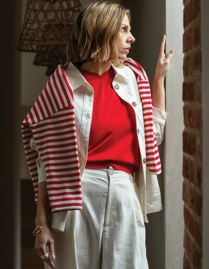 Woman wearing a red and white striped cardigan over a red shirt with white pants, standing indoors.
