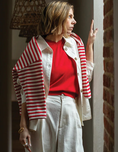 Woman wearing a red and white striped cardigan over a red shirt with white pants, standing indoors.