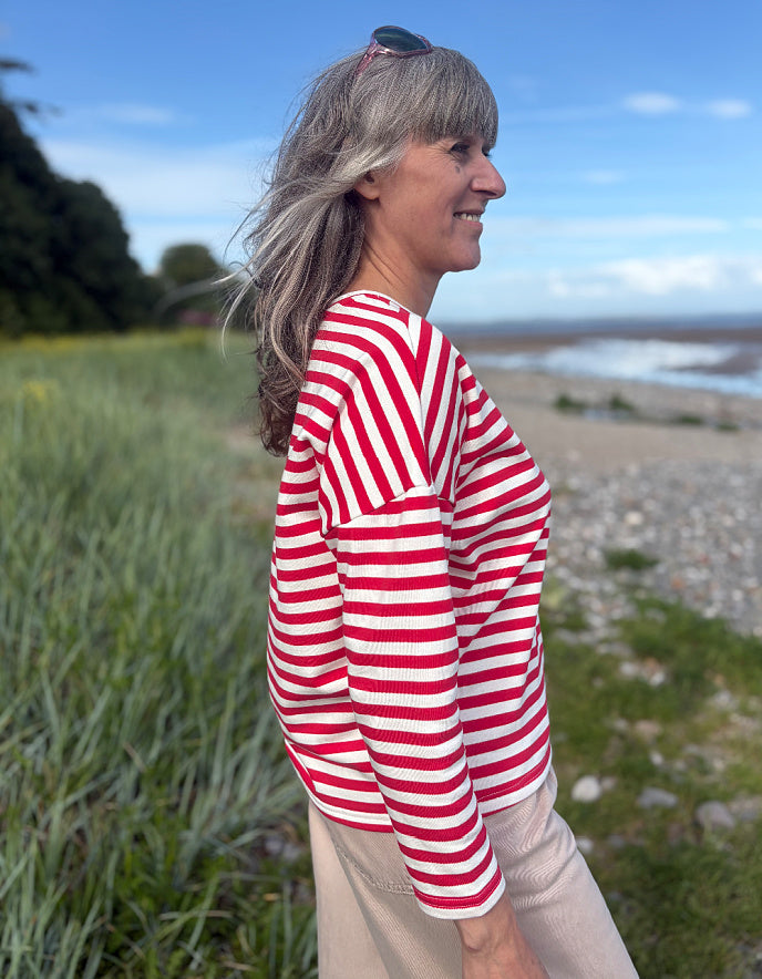 Woman wearing a red and white striped shirt standing outdoors with a scenic background.