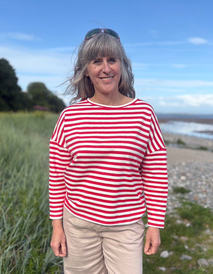 Woman wearing a red and white striped shirt standing outdoors with a scenic background.