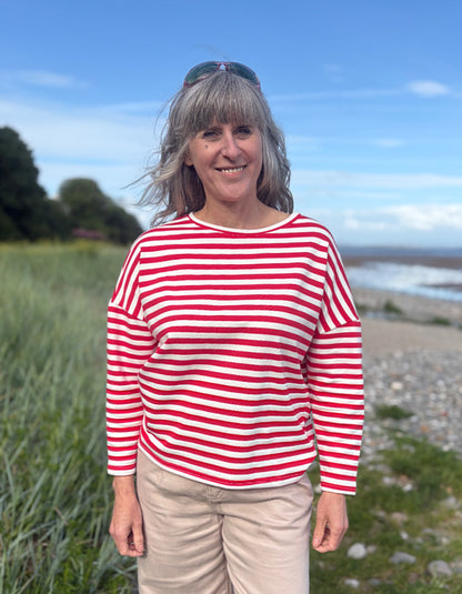 Woman wearing a red and white striped shirt standing outdoors with a scenic background.