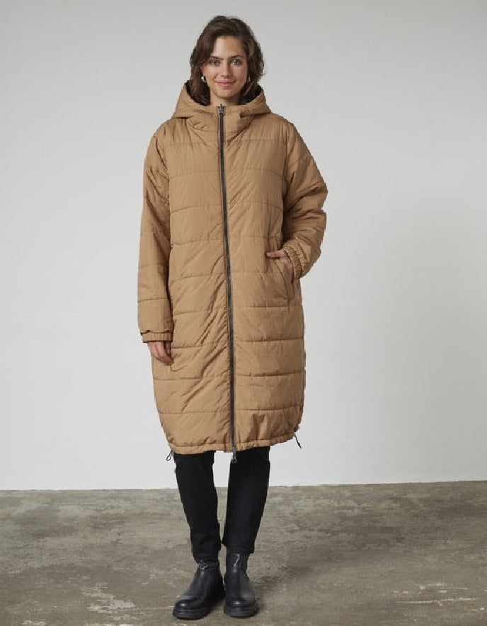 Woman wearing a black and beige reversible winter coat against a plain background