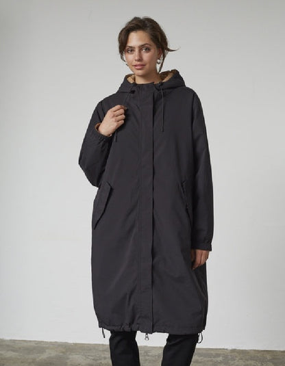 Woman wearing a black and beige reversible winter coat against a plain background