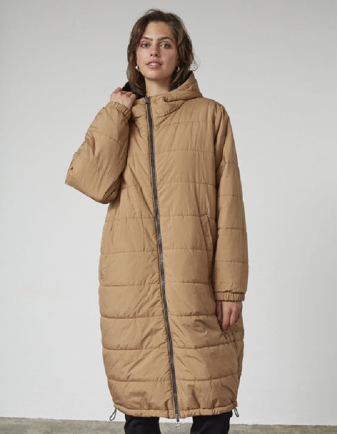 Woman wearing a black and beige reversible winter coat against a plain background