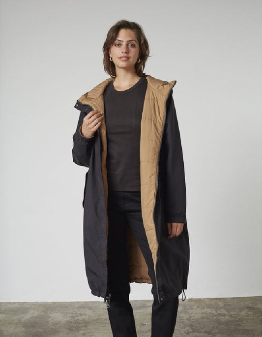 Woman wearing a black and beige reversible winter coat against a plain background