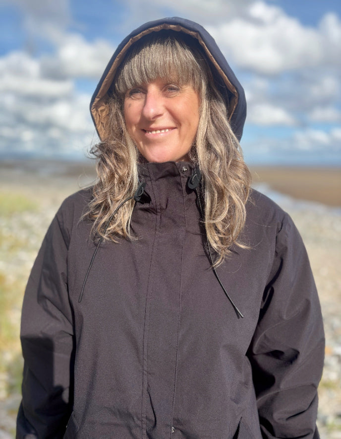 Woman wearing a black and beige reversible winter coat against a plain background