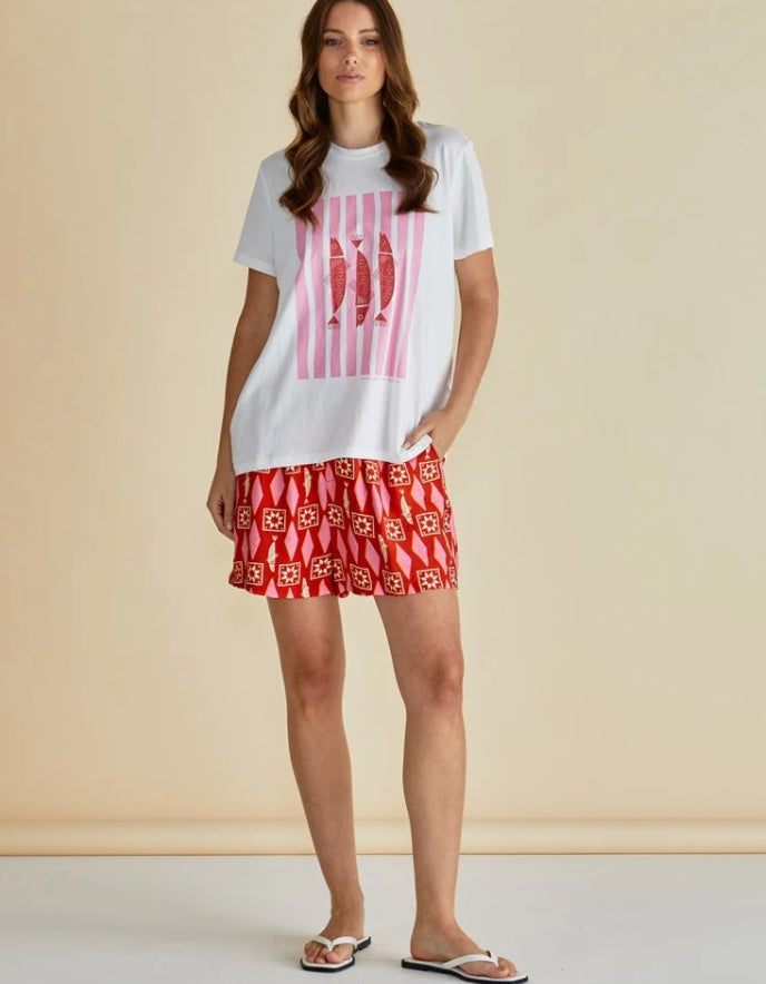 Woman wearing a white t-shirt with a pink design and red patterned shorts on a beige background