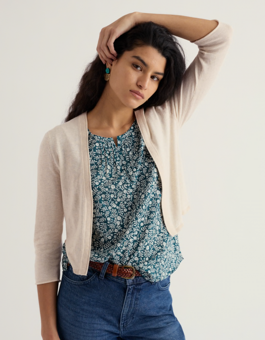 Woman wearing a floral blouse, beige cardigan, and blue jeans on a plain background