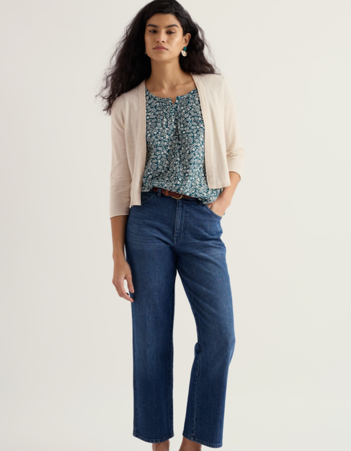 Woman wearing a floral top, beige cardigan, and blue jeans on a white background