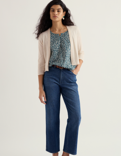 Woman wearing a floral top, beige cardigan, and blue jeans on a white background