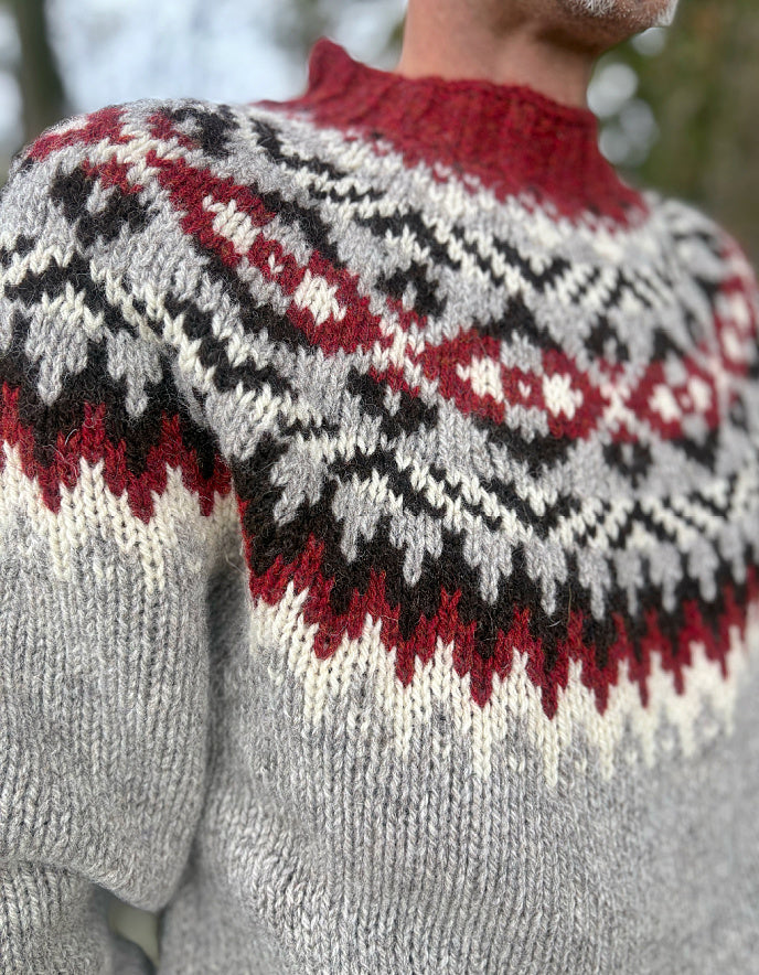 Close-up of a person wearing a patterned sweater with red, black, and white colors.