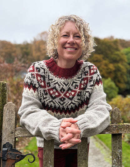 Woman wearing a patterned sweater standing behind a wooden gate with a natural background