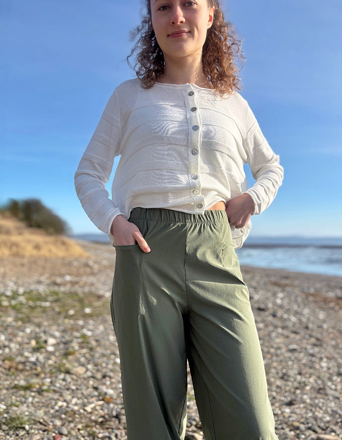 Person wearing green pants and a white shirt on a pebbly beach with ocean view