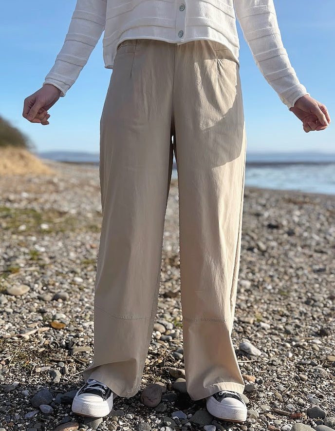 Person wearing beige pants standing on a pebbly beach with a clear sky.