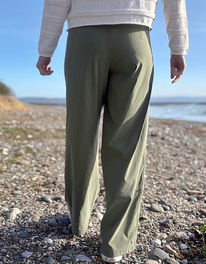 Person wearing green pants standing on a pebbly beach with a clear sky.