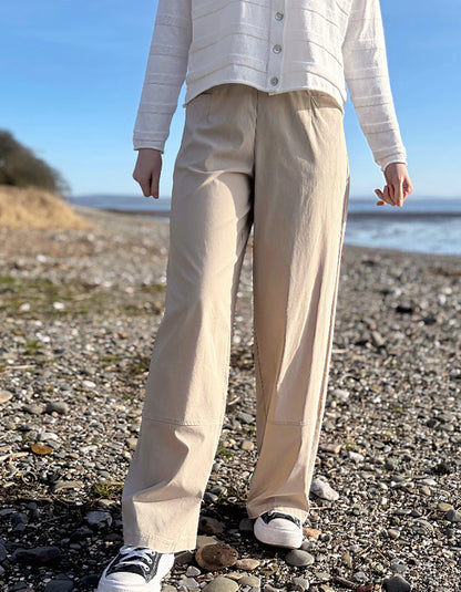 Person wearing beige pants and a white shirt on a pebbly beach.