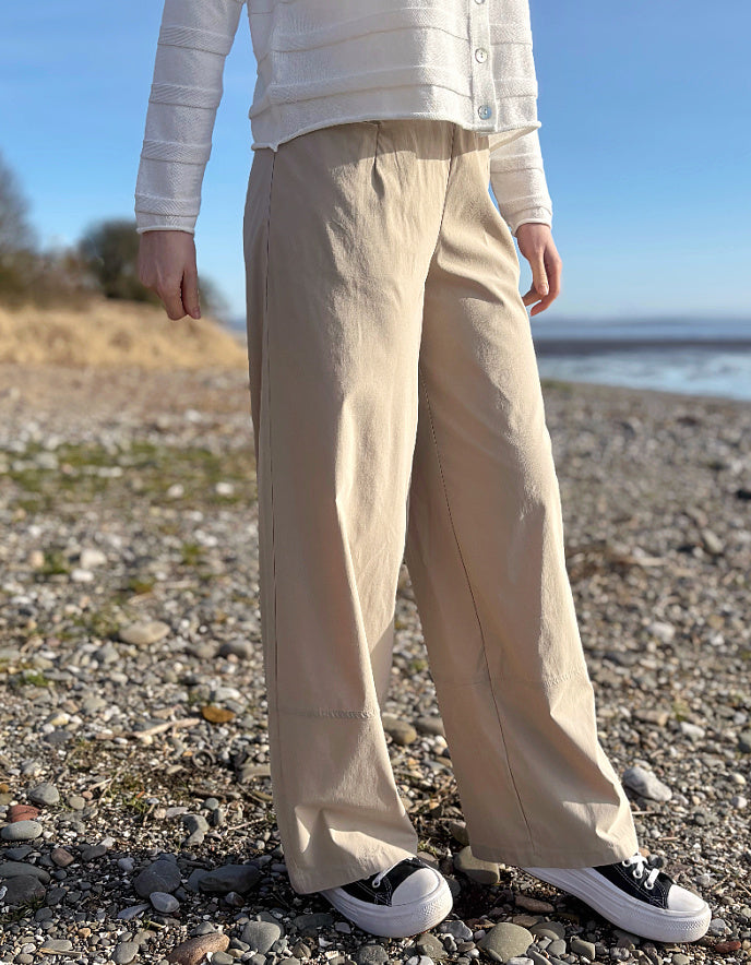 Person wearing beige pants and a white shirt on a pebbly beach.