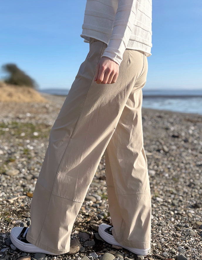 Person wearing beige pants standing on a pebbly beach with a clear sky.