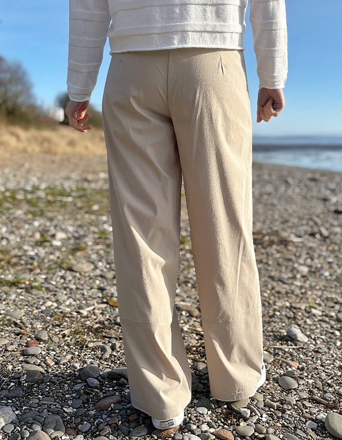 Person wearing beige pants standing on a pebbly beach with a blurred background