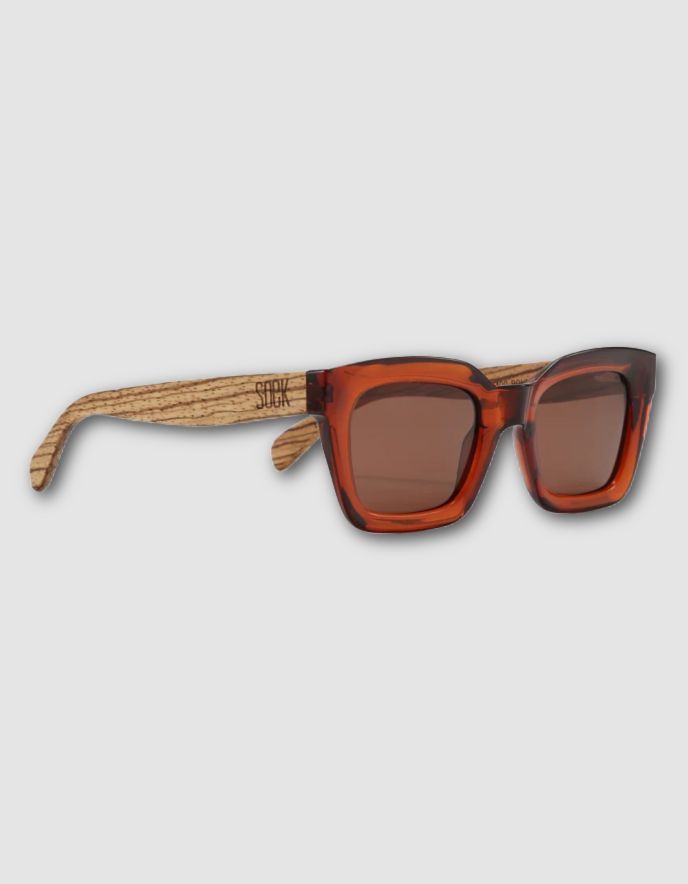 Square sunglasses with translucent amber-brown frames, brown tinted lenses, and light natural wood temples with a visible 'SOL' logo, shown on a light gray background.