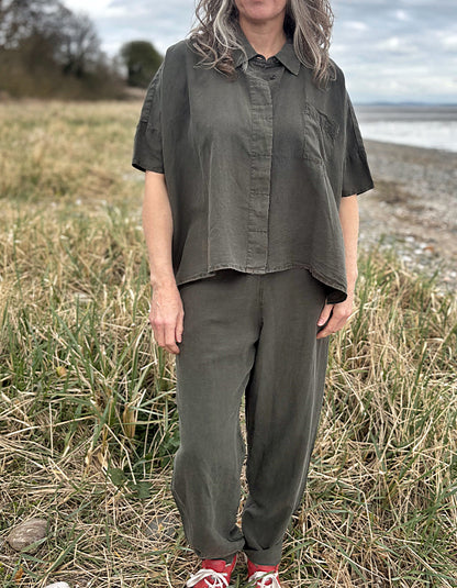 Person standing in a field wearing a green tencel oversized shirt, white pants, and red sneakers.