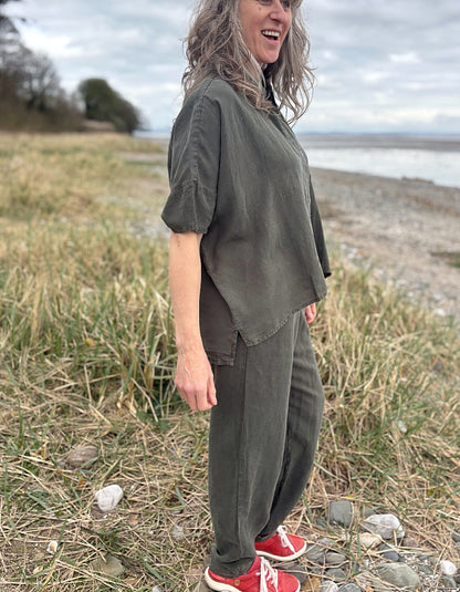 Person standing in a field wearing a green tencel oversized shirt, white pants, and red sneakers.