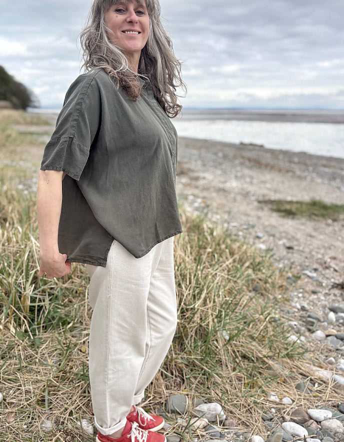 Person standing in a field wearing a green tencel oversized shirt, white pants, and red sneakers.