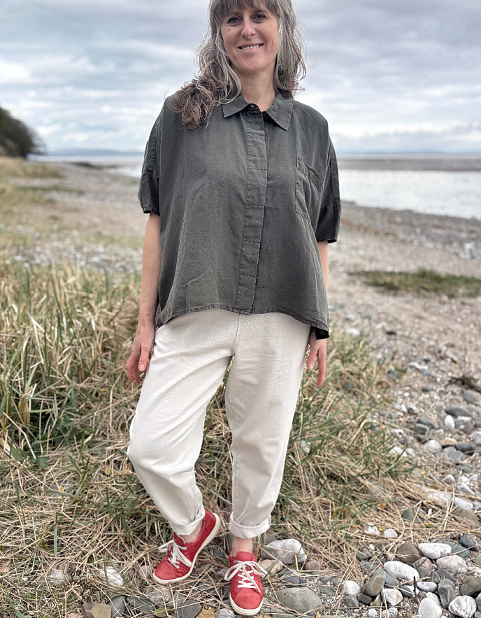 Person standing in a field wearing a green tencel oversized shirt, white pants, and red sneakers.