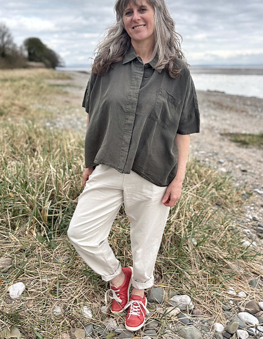 Person standing in a field wearing a green tencel oversized shirt, white pants, and red sneakers.